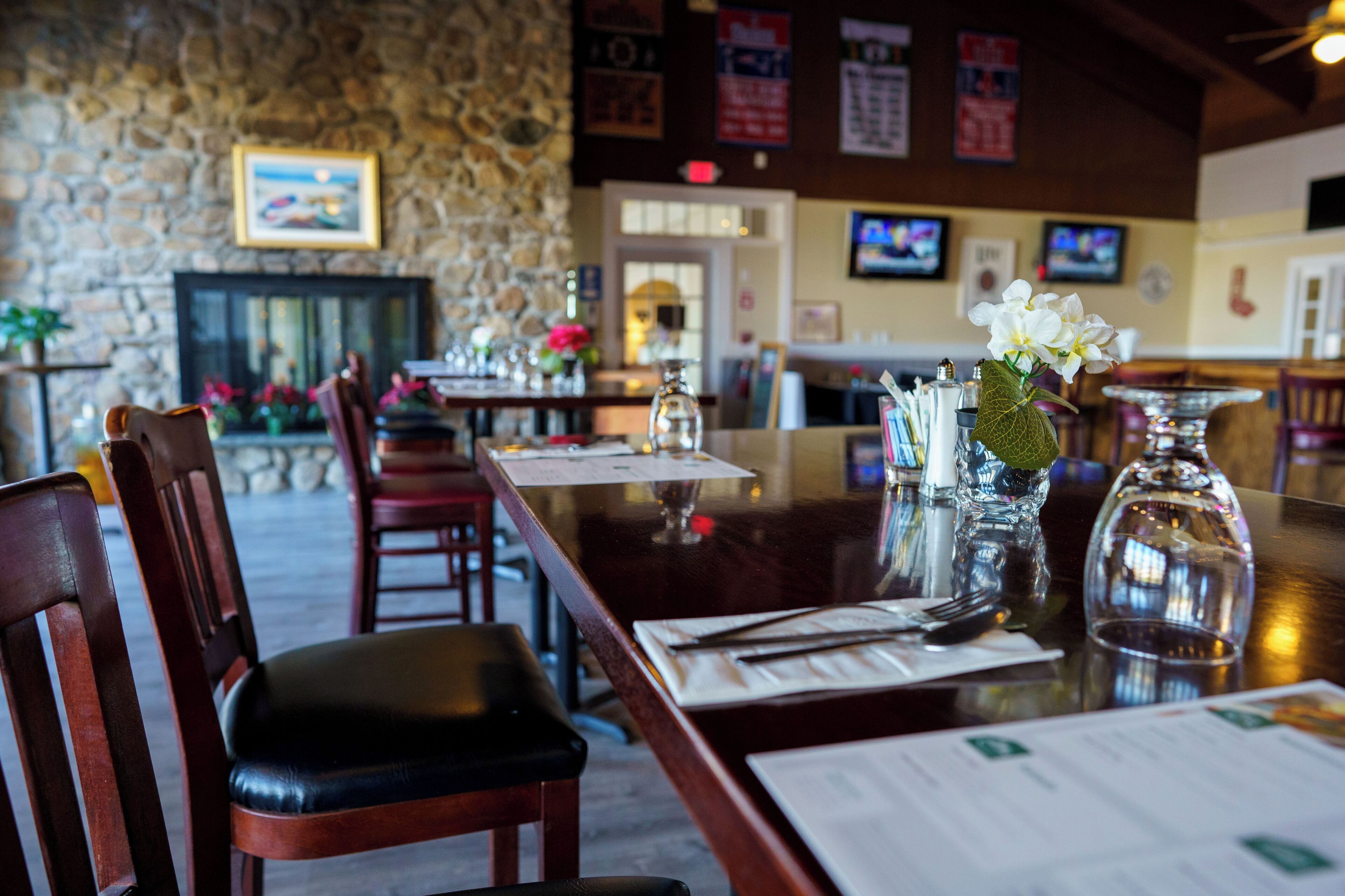 A restaurant with stone walls, wooden chairs, and tables set for dining.