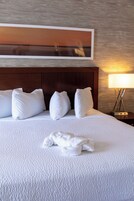 A neatly made bed with white linens and pillows, a wooden headboard, and a wall-mounted picture.