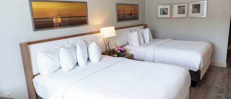 A hotel room with two beds, a nightstand with a lamp, and three framed pictures on the wall.