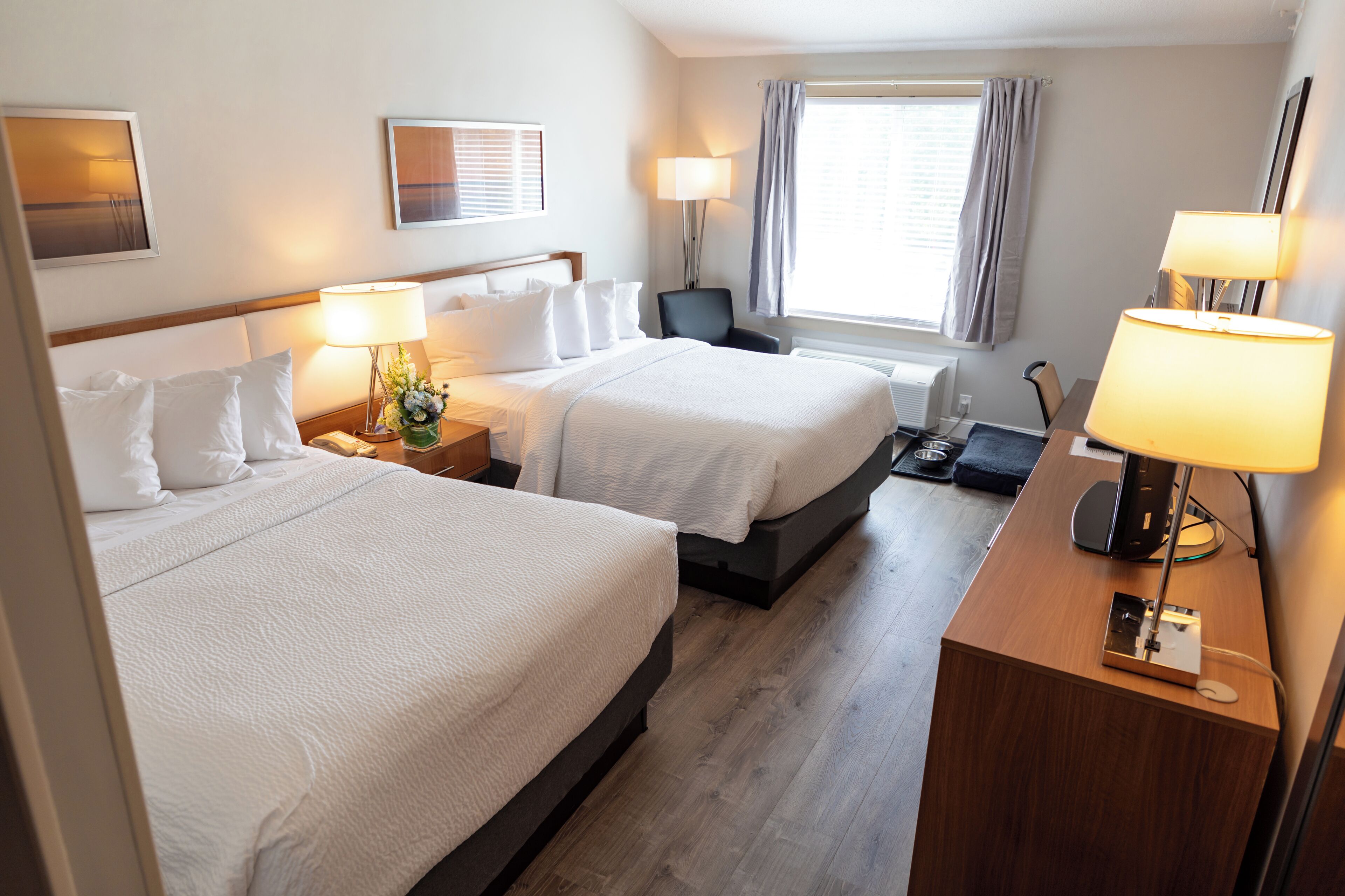 A hotel room with two beds, a desk, a chair, a lamp, and a window with curtains.