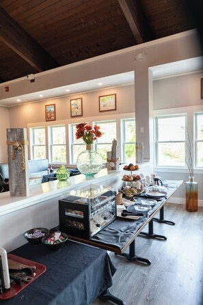 A long dining table with a glass centerpiece, surrounded by chairs and a buffet setup. - Iris Hotel Cape Cod  (Falmouth)