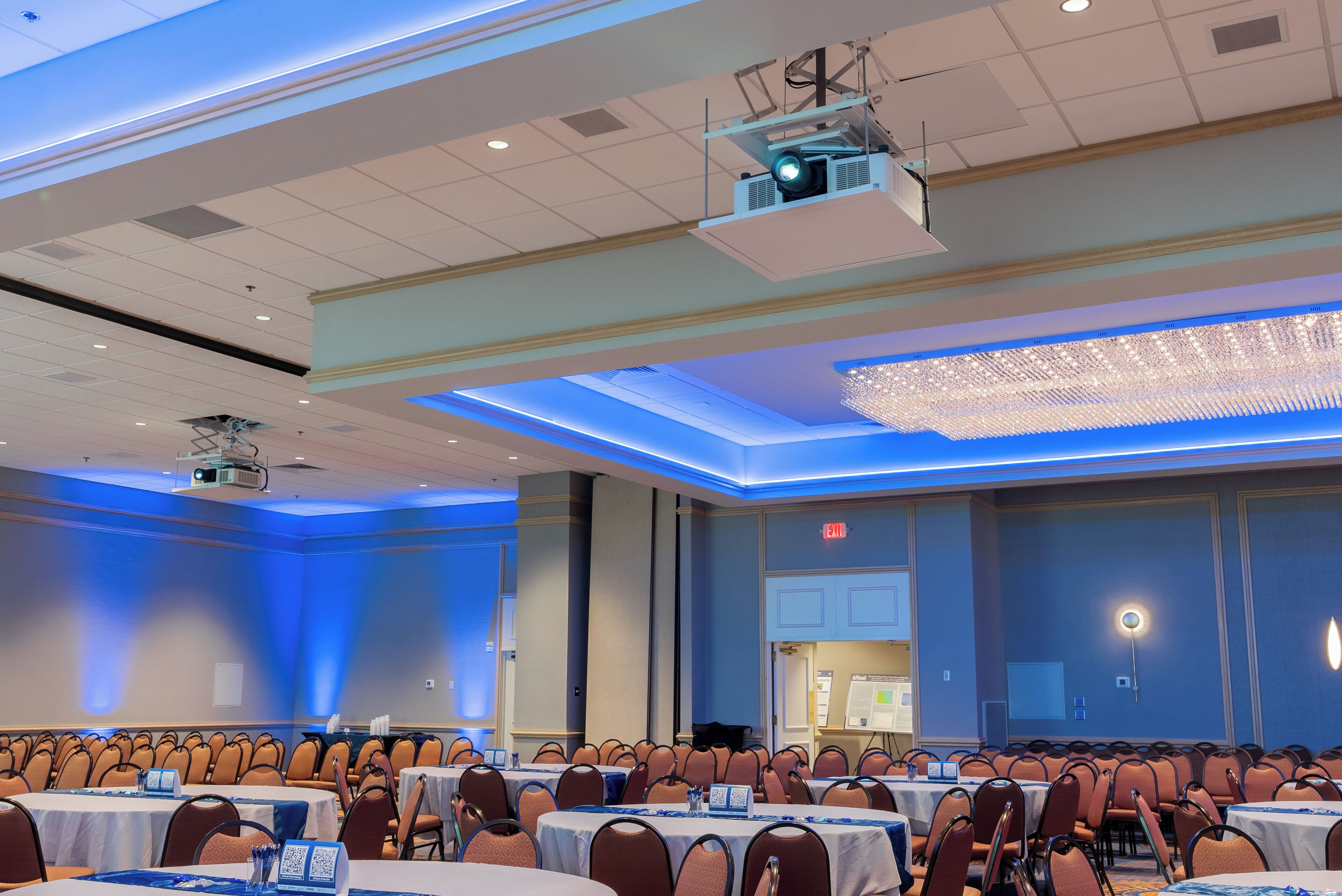 A conference room with rows of tables and chairs, a projector, and a chandelier.