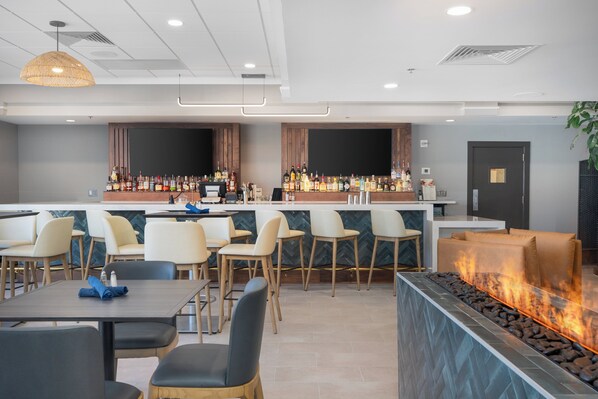 A modern bar area with a long counter, multiple seating options, and a built-in fire feature.
