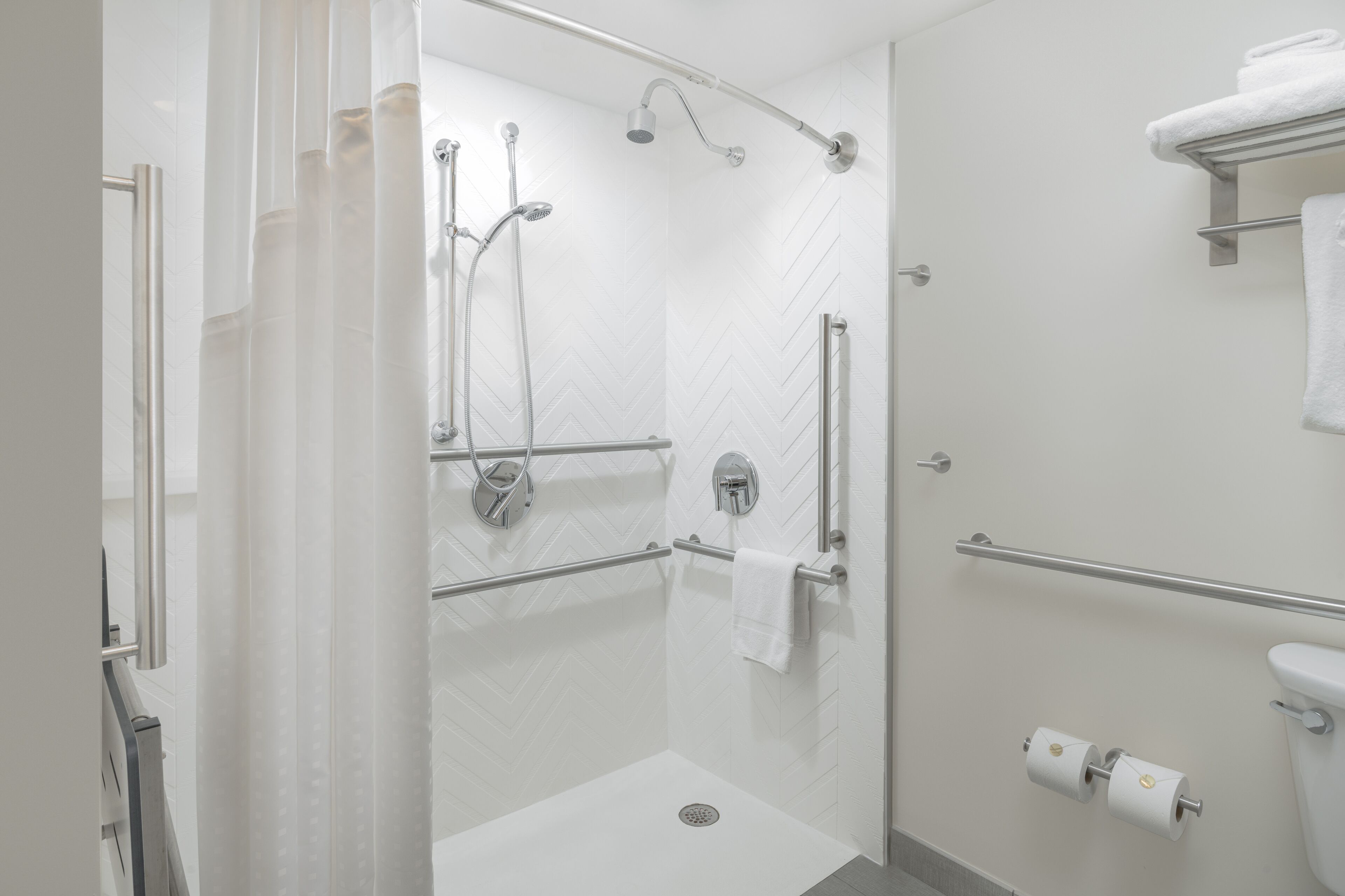 Ein modernes Badezimmer mit bodenebenen Dusche, Haltegriffen, Toilette und Handtuchhalter.