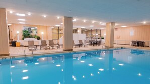 A swimming pool with lounge chairs and tables, surrounded by a well-lit indoor area with a view of the outside. - Holiday Inn Portland-By the Bay by IHG (Portland)