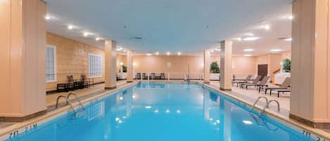 An indoor swimming pool with clear water, surrounded by lounge chairs and a tiled floor.