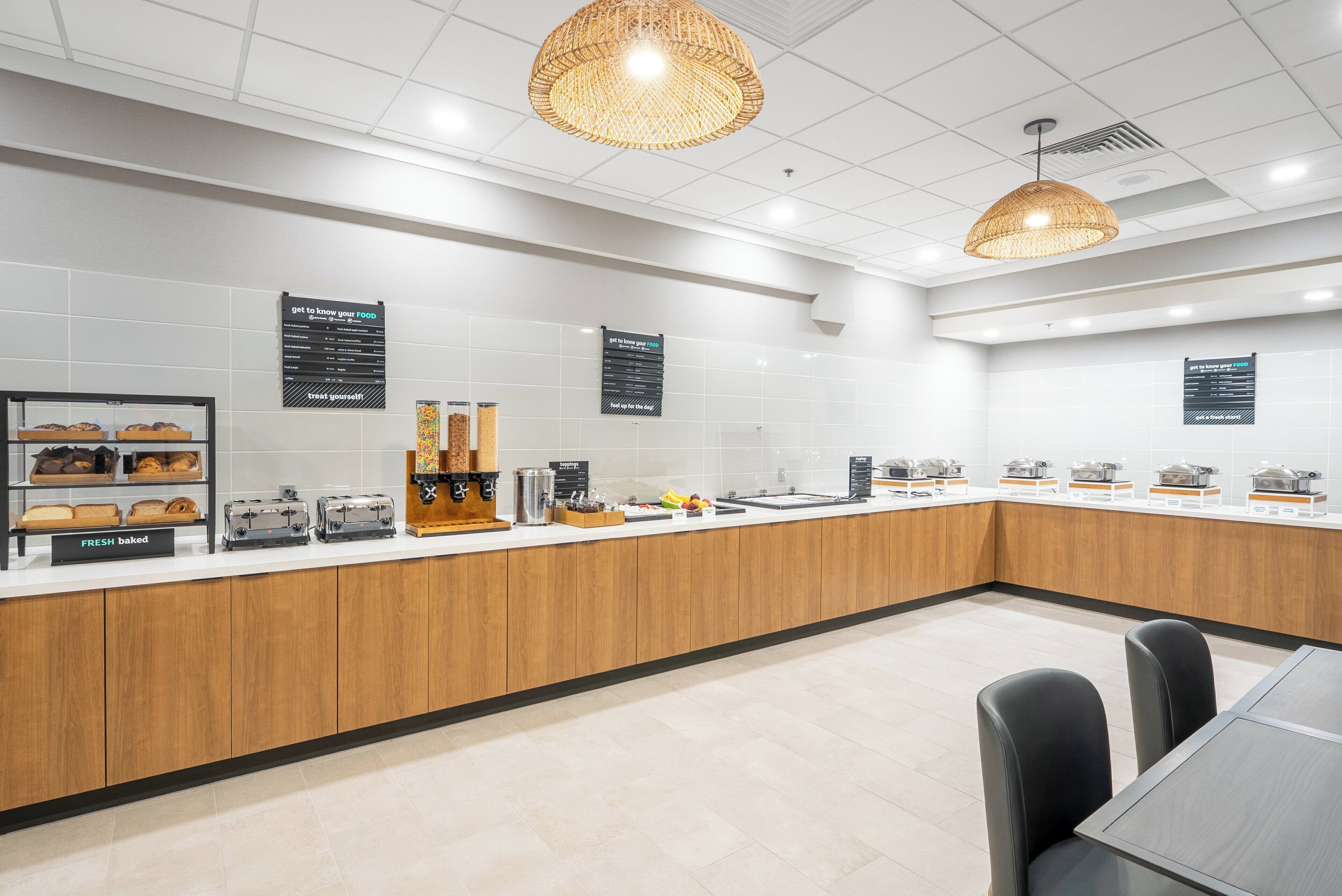 A modern breakfast area with a long counter, various food stations, and seating.