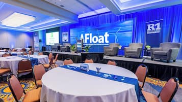 A conference room with round tables, chairs, and a stage with a presentation screen.