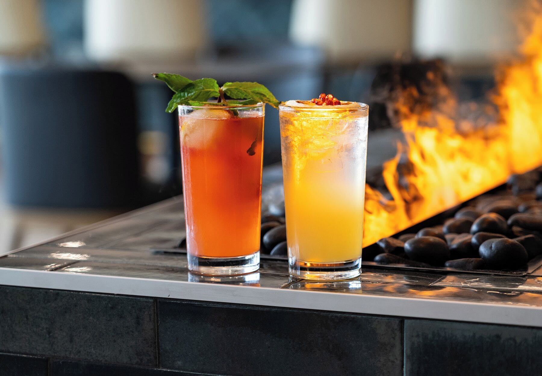 Two drinks on a bar counter with a fire in the background.
