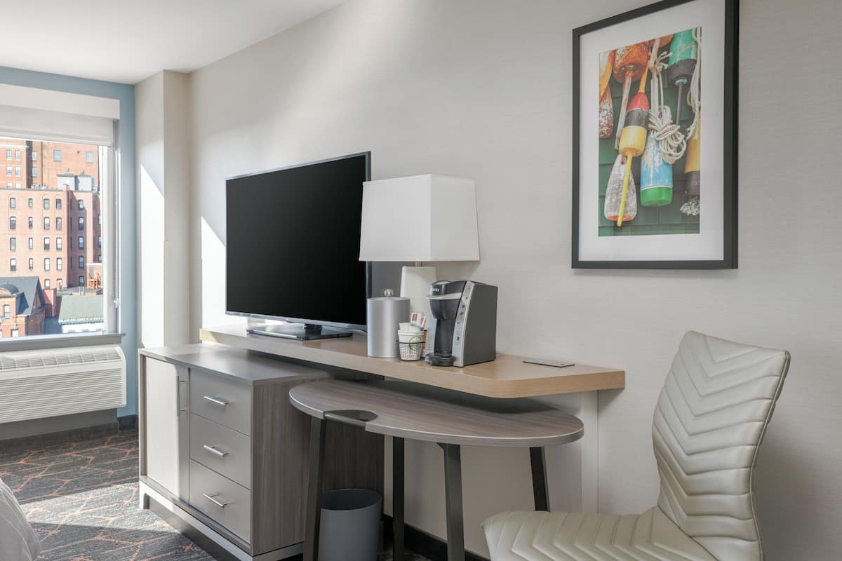 A hotel room with a flat-screen TV, a coffee maker, a framed artwork, and a chair.