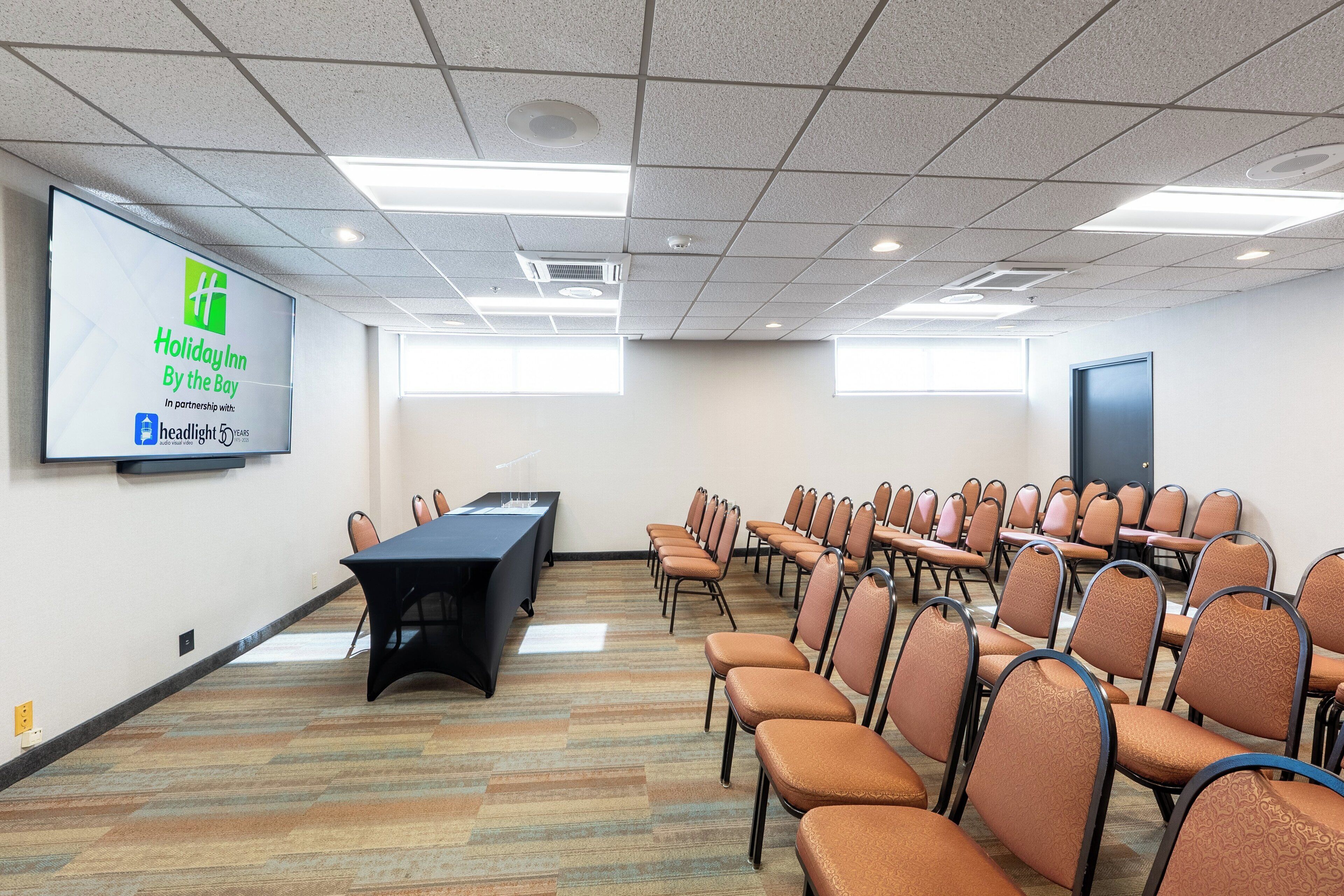 A conference room with a presentation screen, a long table, and rows of chairs.