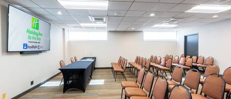 A conference room with a presentation screen, a long table, and rows of chairs.
