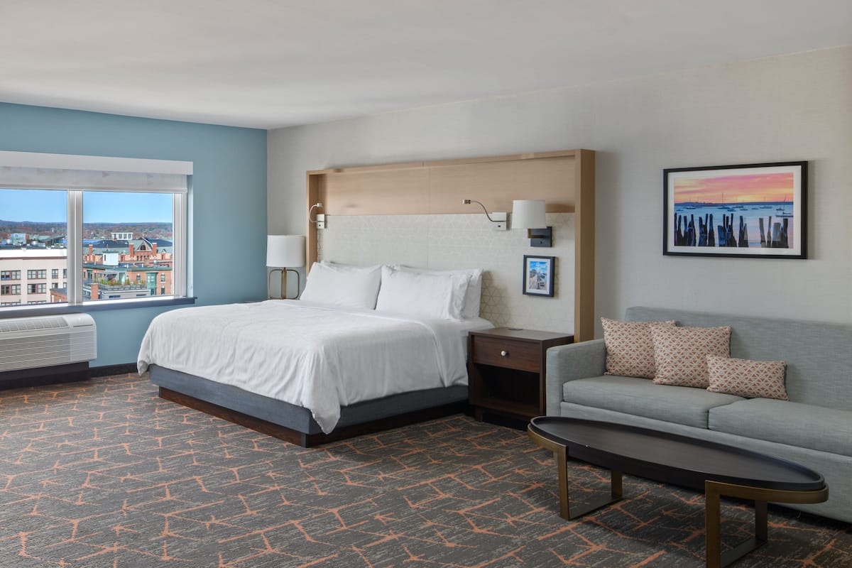 A hotel room with a bed, a sofa, a coffee table, and a view of the city.