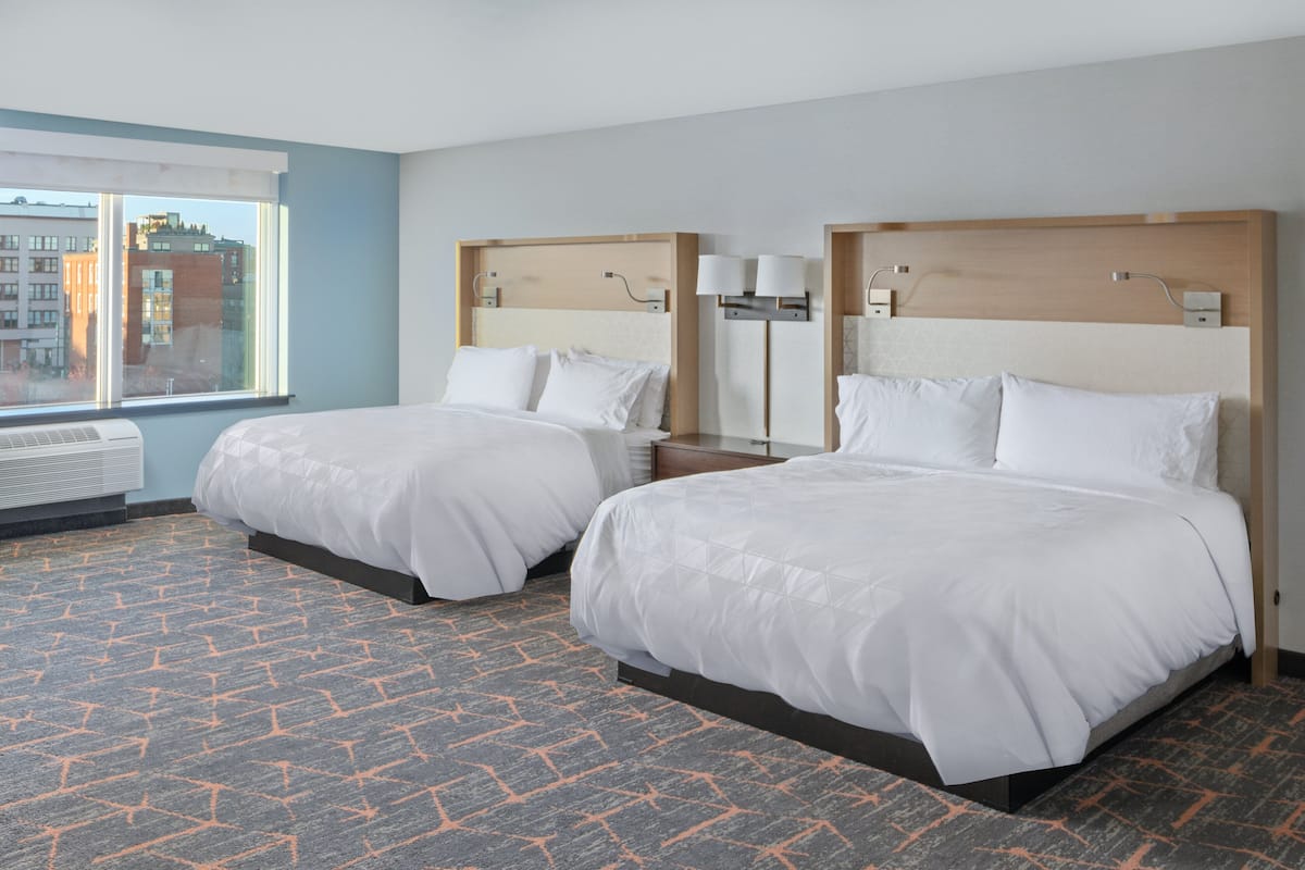 A hotel room with two beds, a large window, and a patterned carpet.