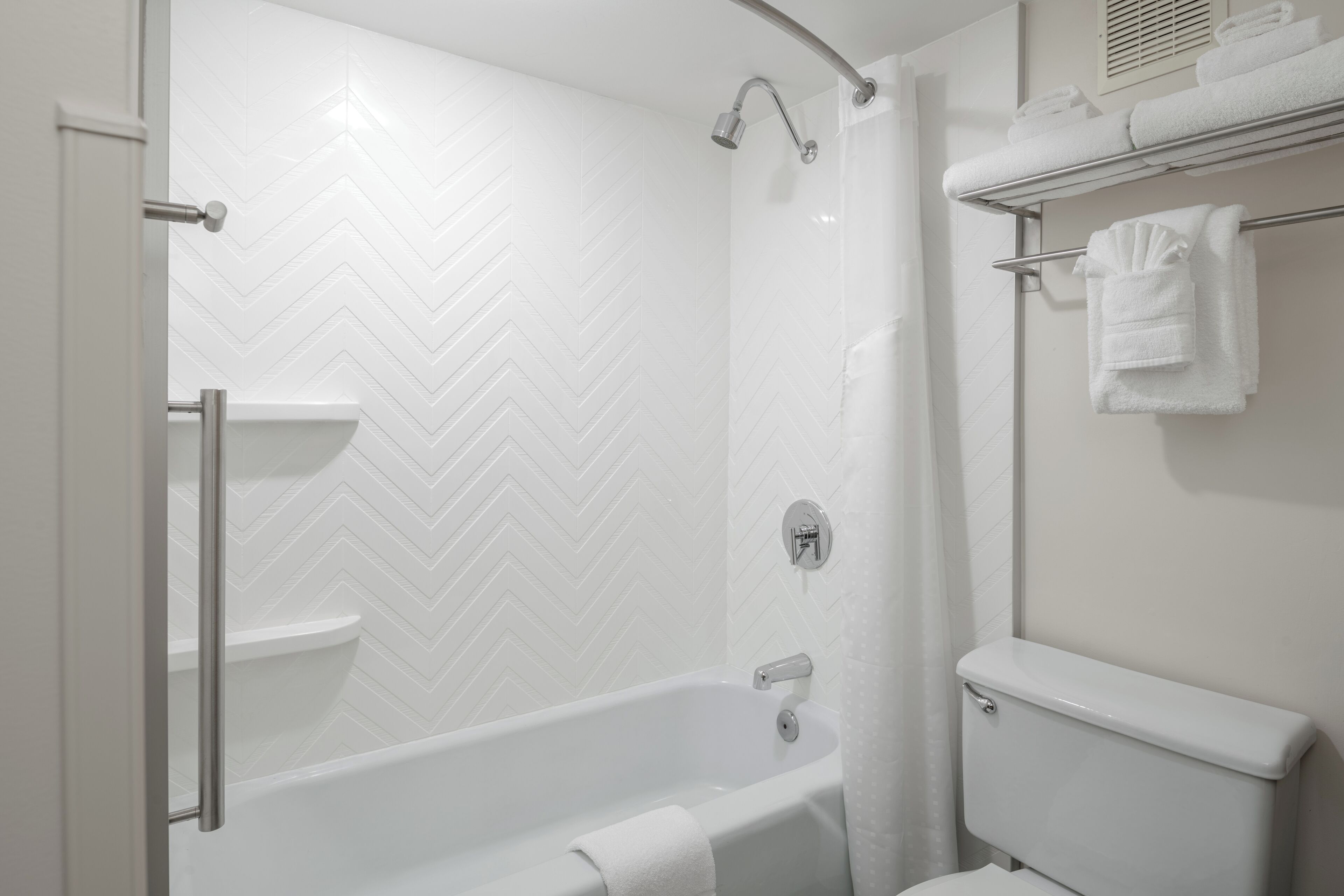 A modern bathroom with a white herringbone tile wall, a freestanding bathtub, a toilet, and a towel rack with folded towels.