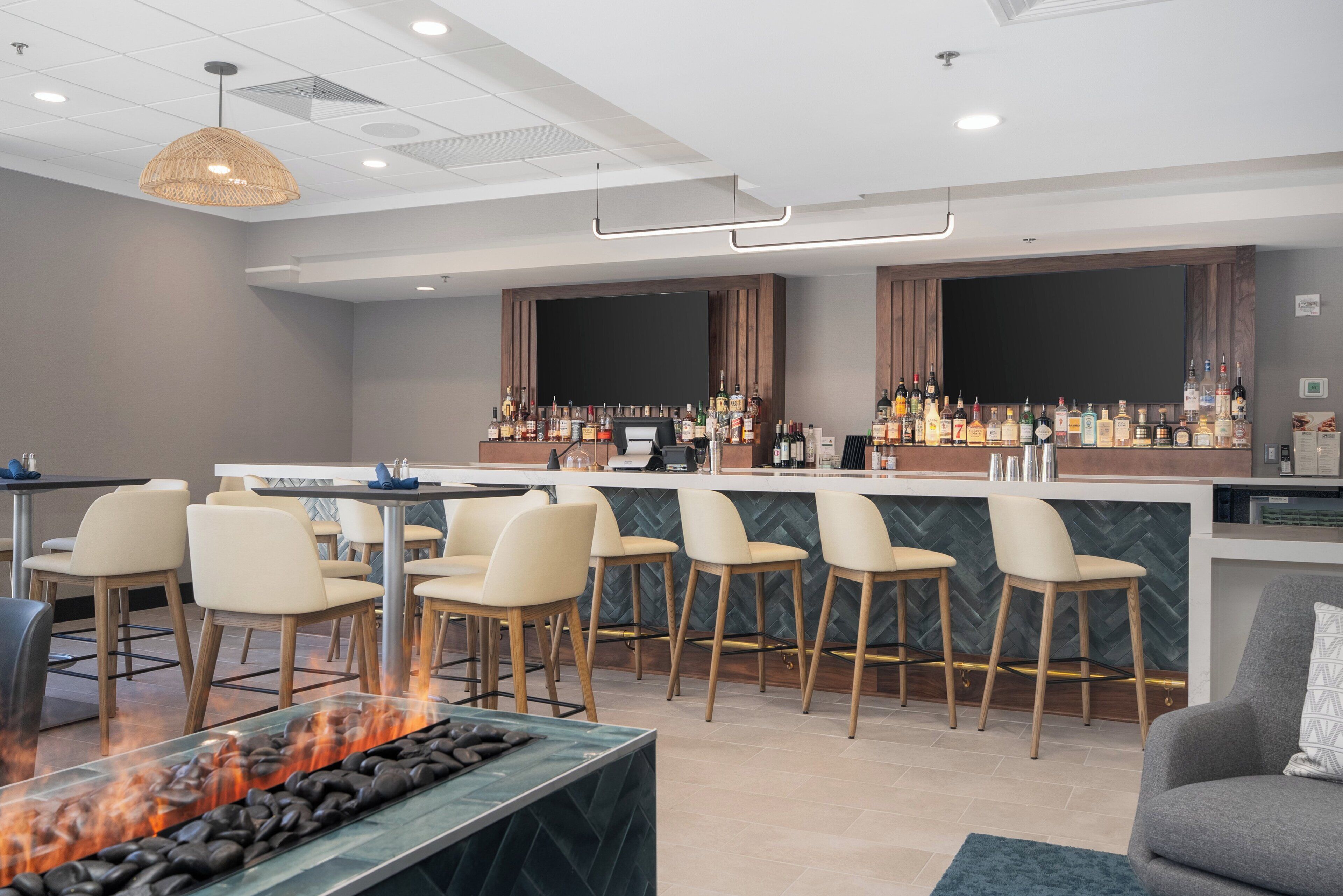 A bar area with a long counter, multiple stools, and a fire feature in the foreground.