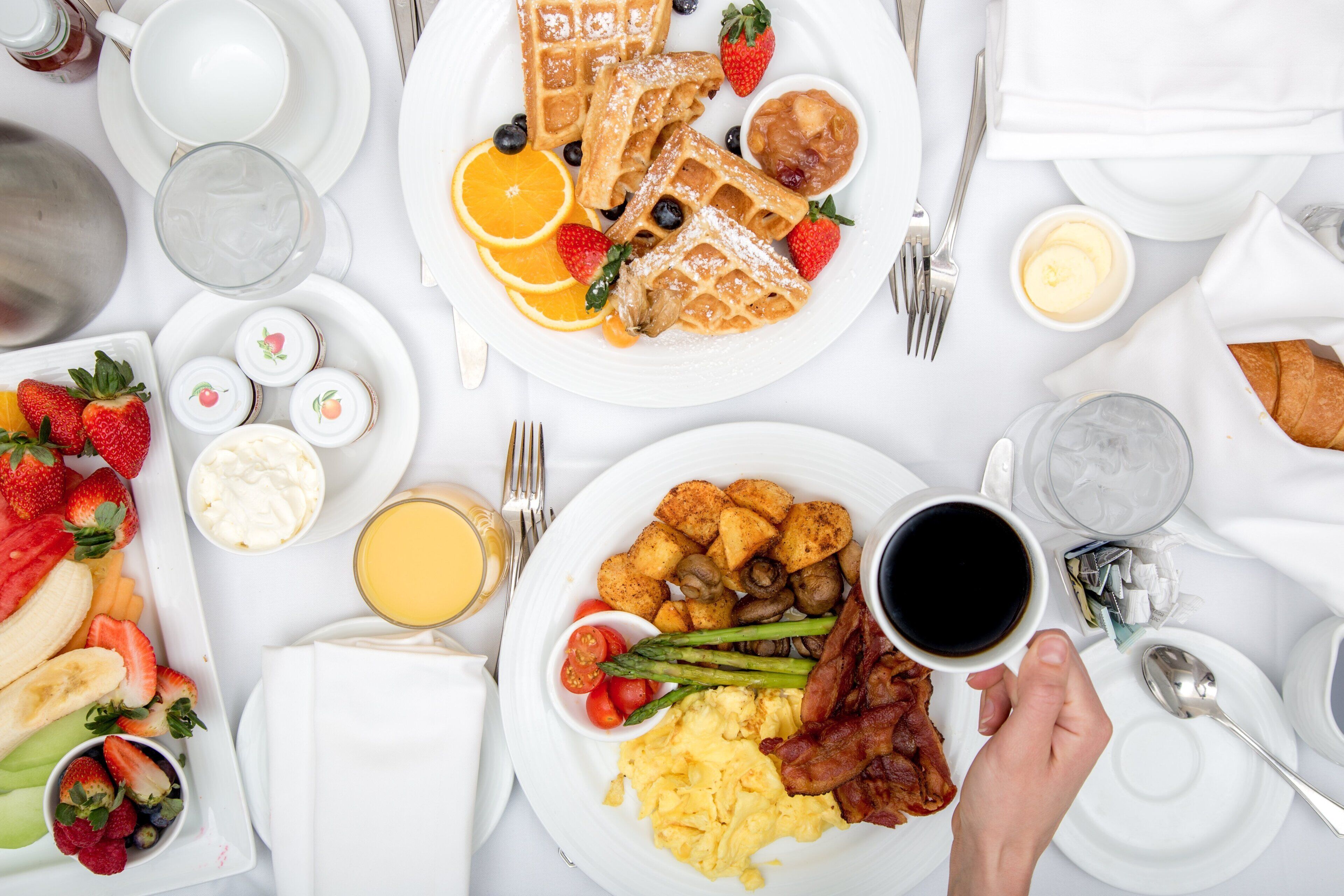 A breakfast setting with waffles, fruit, scrambled eggs, bacon, and toast.