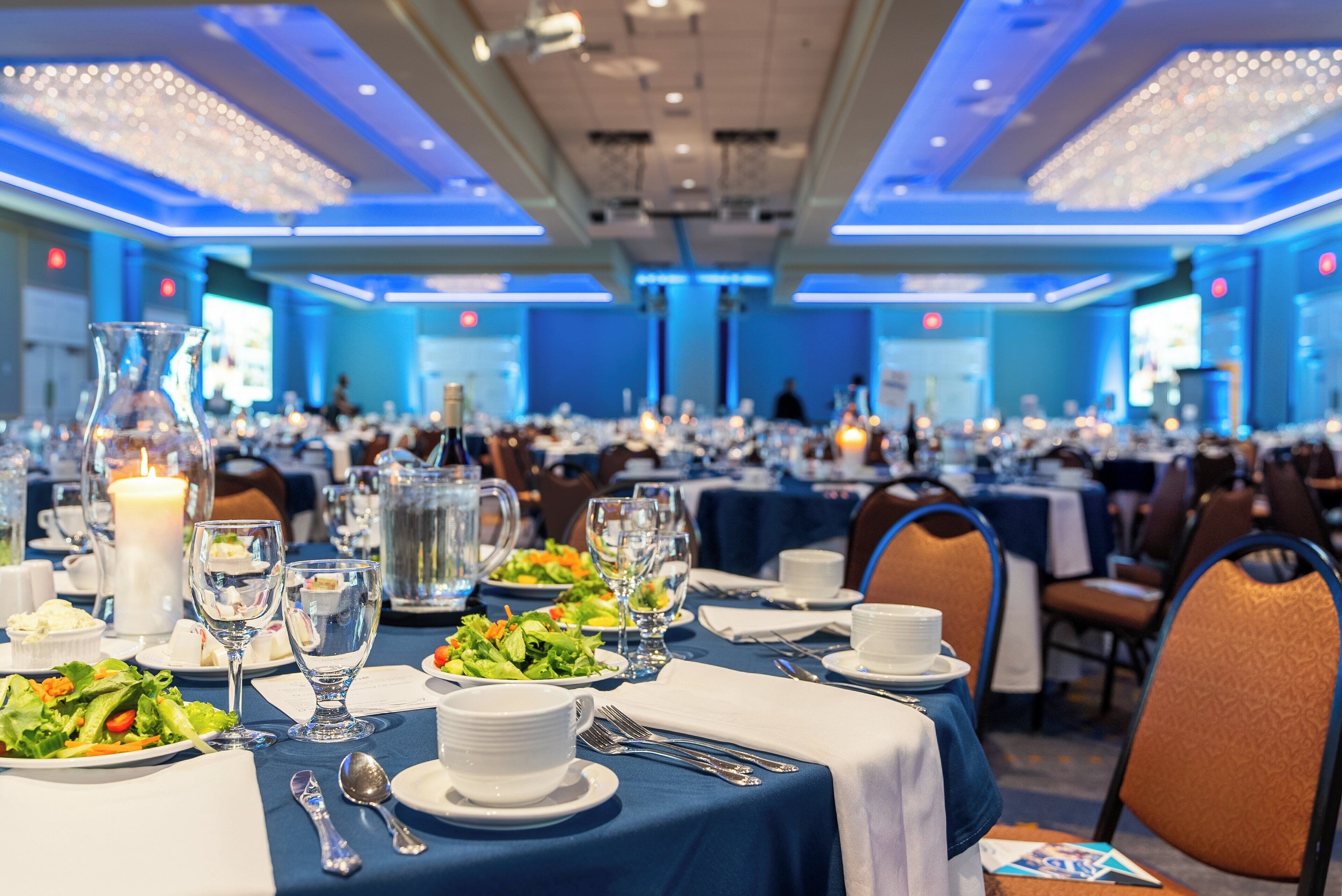 A banquet hall with tables set for a formal event, featuring blue tablecloths, white plates, and clear glassware.