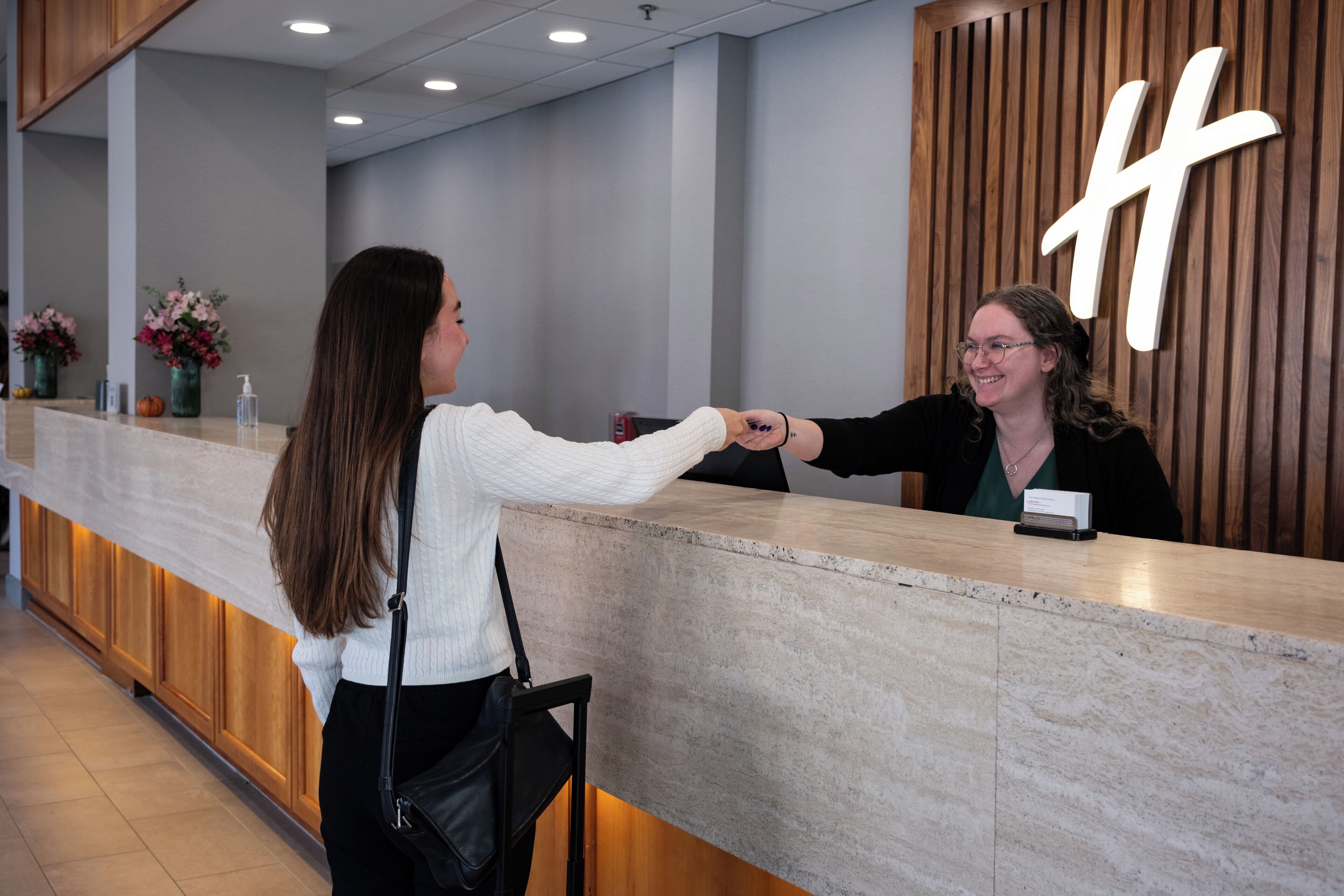 A reception area with a wooden reception desk, a large illuminated 'H' sign, and a vase with flowers on the counter.