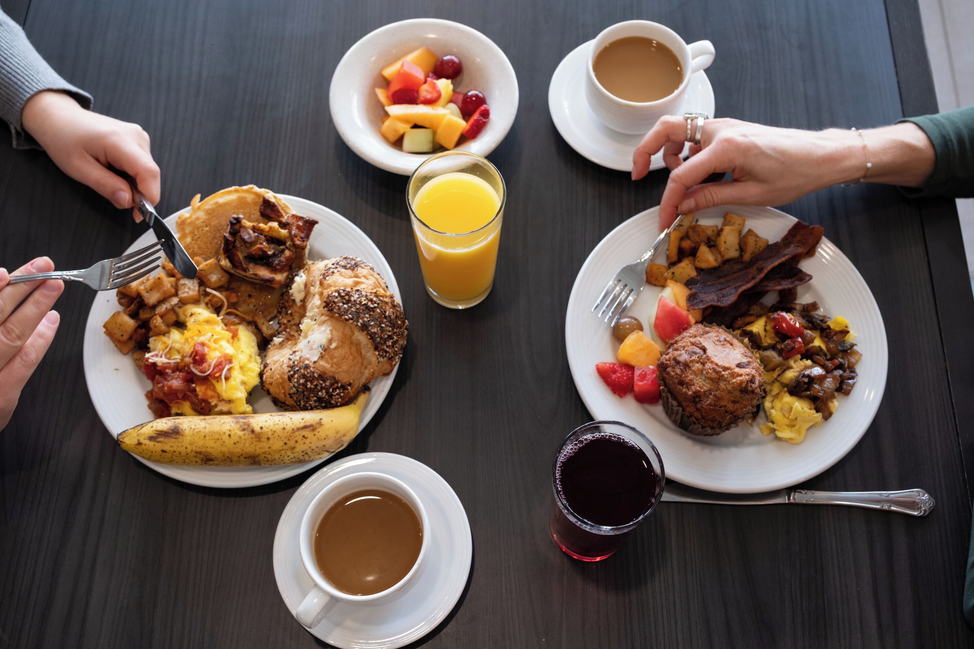 A breakfast setting with various dishes, including pancakes, eggs, and fruits, on a wooden table.