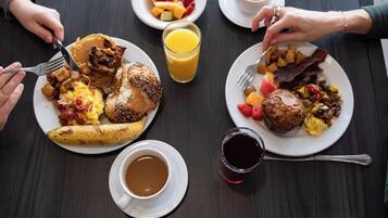 A breakfast setting with various dishes, including pancakes, eggs, and fruits, on a wooden table.