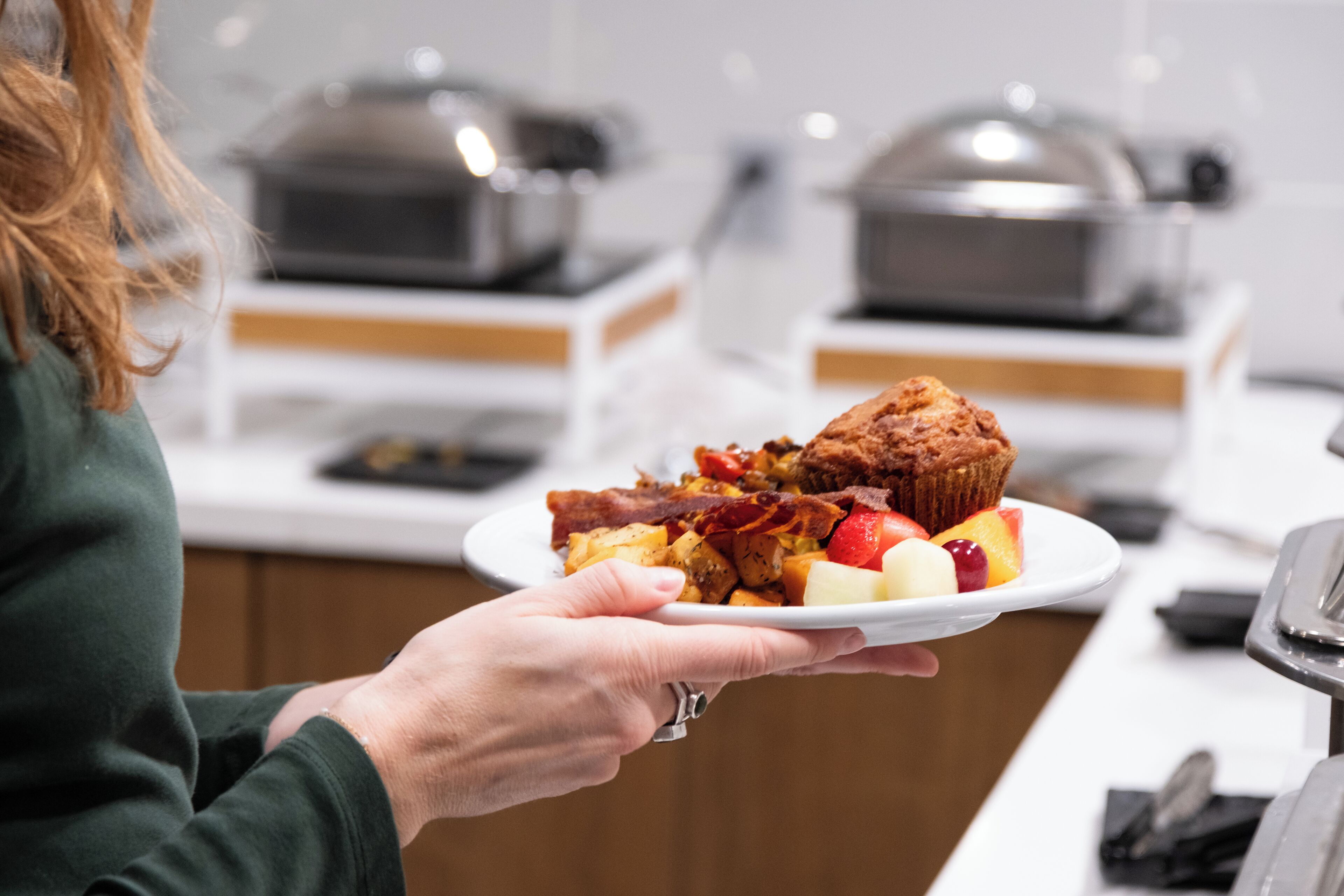 Uma pessoa segurando um prato com comida, incluindo um muffin, bacon e frutas.