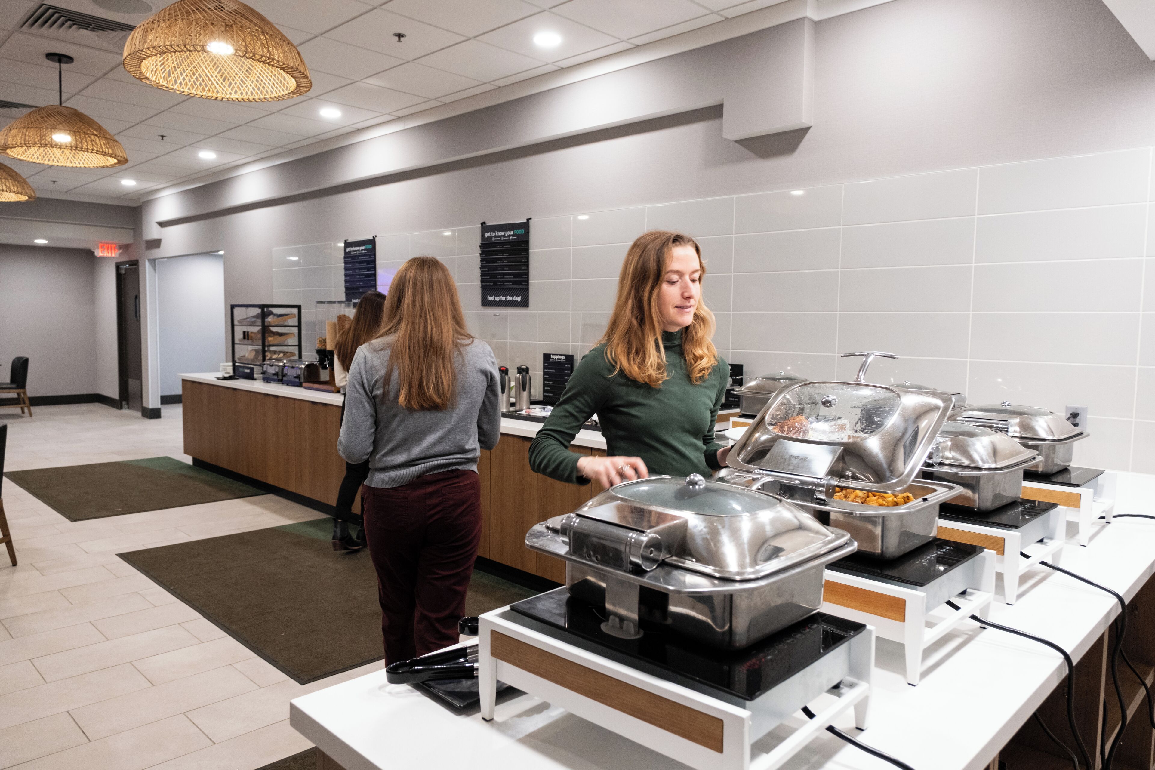 Un espace buffet avec plusieurs points de service, un comptoir d’accueil et un mur recouvert de carreaux sur lequel sont affichés des panneaux.