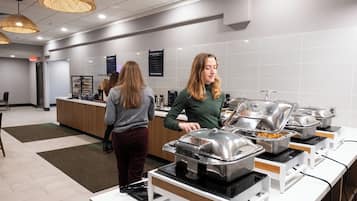 Un espace buffet avec plusieurs points de service, un comptoir d’accueil et un mur recouvert de carreaux sur lequel sont affichés des panneaux.