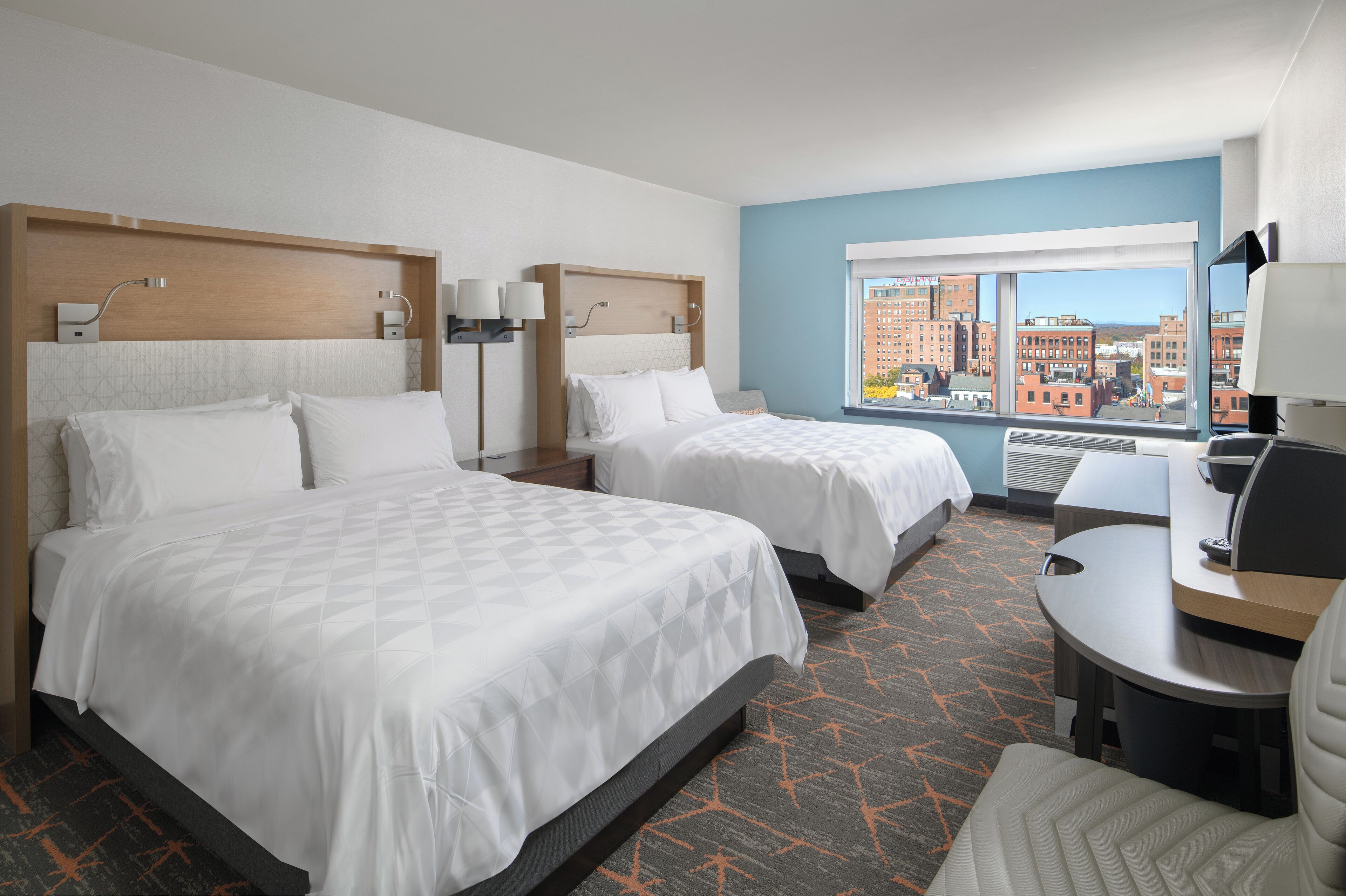 Een hotelkamer met twee bedden, een bureau en uitzicht op de stad.