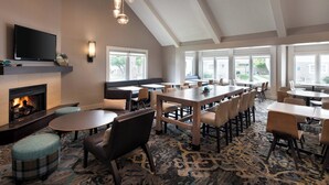 A spacious dining area with multiple tables and chairs, a fireplace, and large windows providing natural light. - Residence Inn By Marriott Boulder (Boulder)