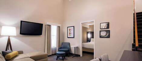 Habitación de hotel con sofá, sillón, reposapiés, una mesita, televisor y ventilador de techo.
