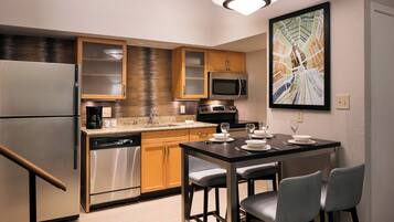 A modern kitchen with a refrigerator, microwave, and dishwasher. There is a dining table with chairs and a painting on the wall.