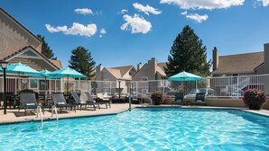 A swimming pool with lounge chairs and umbrellas, surrounded by a fence and trees. - Residence Inn By Marriott Boulder (Boulder)