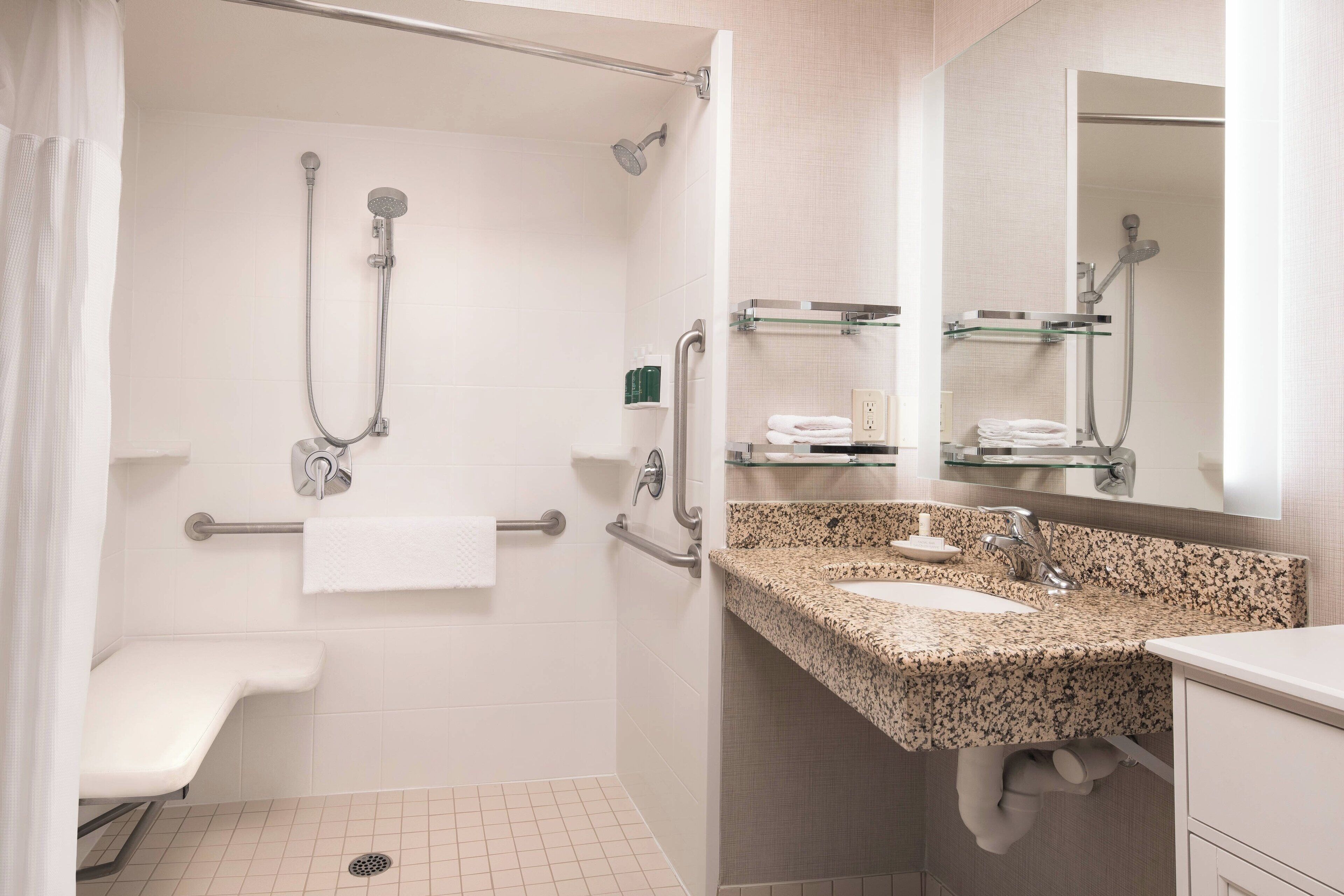 Un baño moderno con ducha, barras de apoyo, lavamanos y espejo.