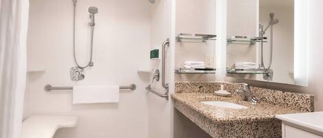 A modern bathroom with a shower, grab bars, a sink, and a mirror.