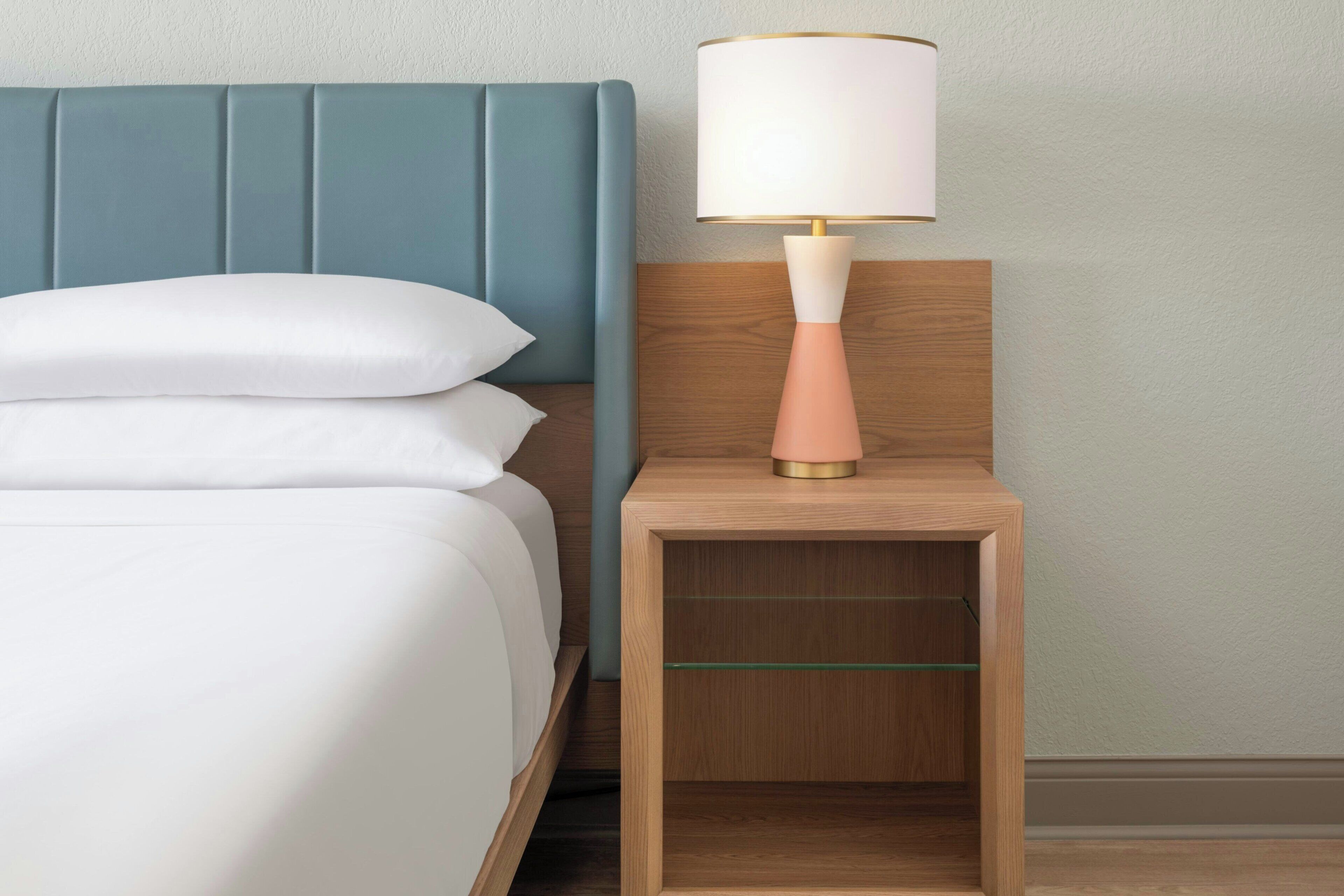 A bed with a blue headboard, a bedside table with a lamp, and a wooden nightstand.