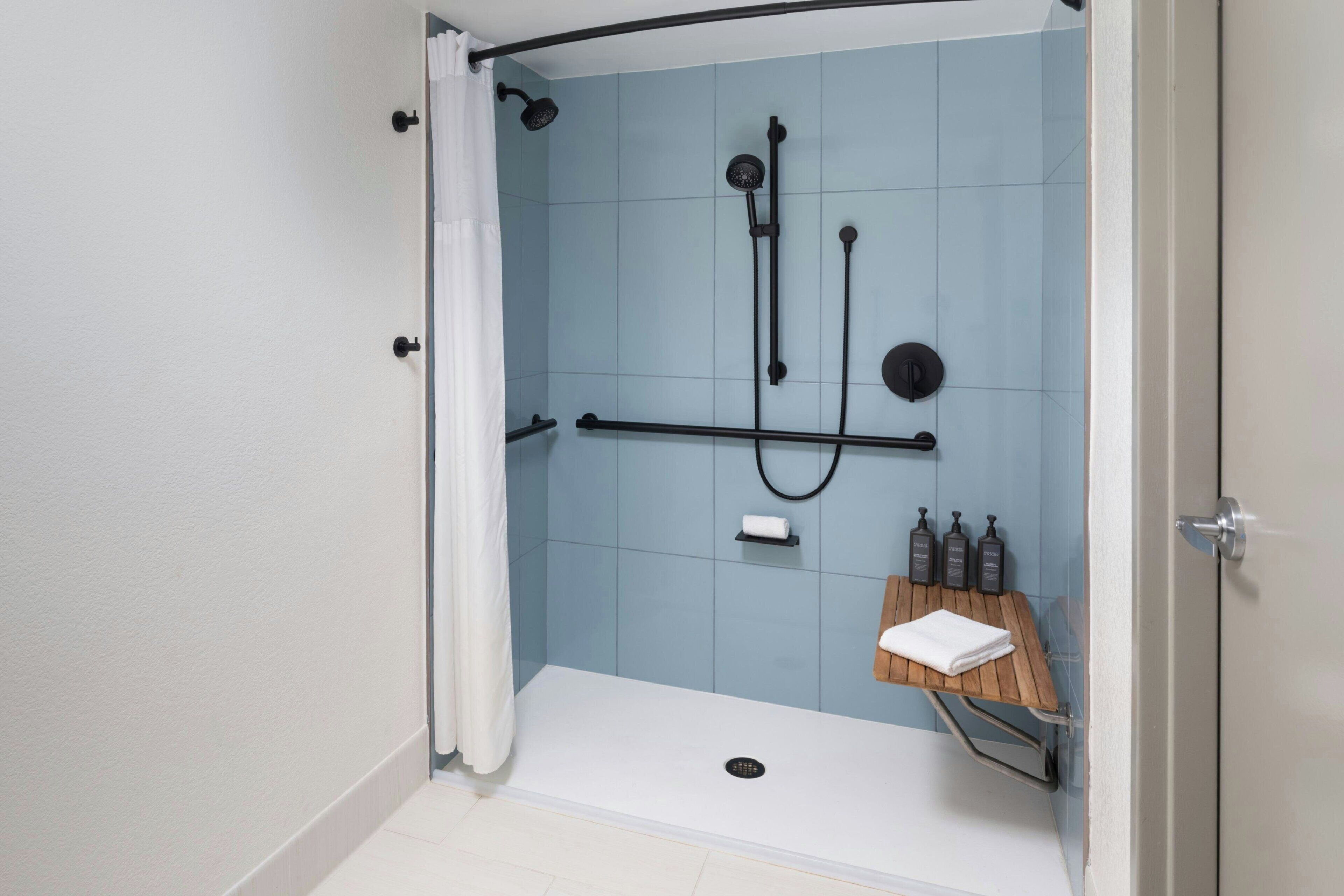 A shower with a white curtain, a handheld showerhead, a wall-mounted faucet, and a small shelf with toiletries.