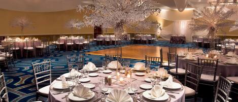 A banquet hall with round tables set for dining, featuring white tablecloths and silverware.