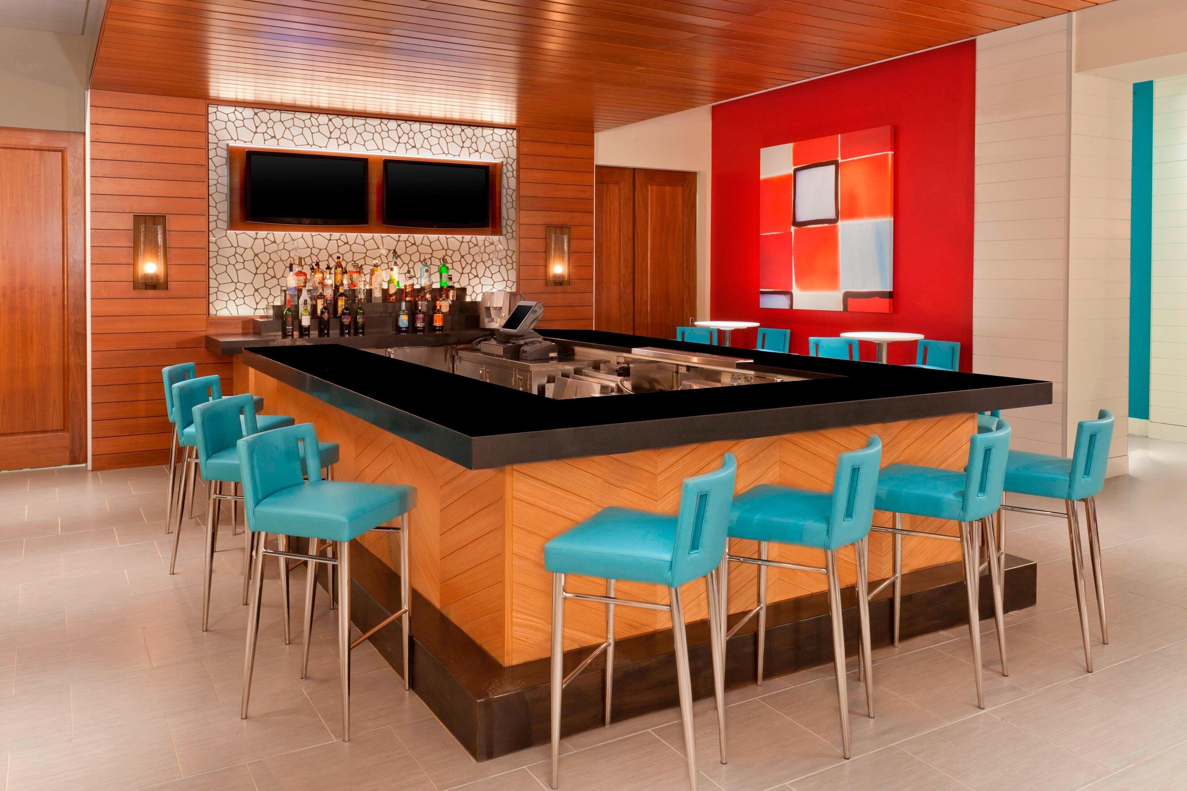 A modern bar area with a central island, bar stools, a TV mounted on the wall, and a red accent wall.