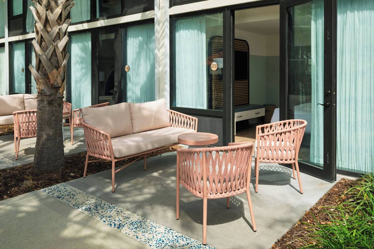 A modern outdoor seating area with wicker furniture, a palm tree, and a building with large windows and a glass door.