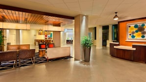 Un hall d’hôtel moderne avec un comptoir d’accueil, un espace salon et une grande plante en pot.