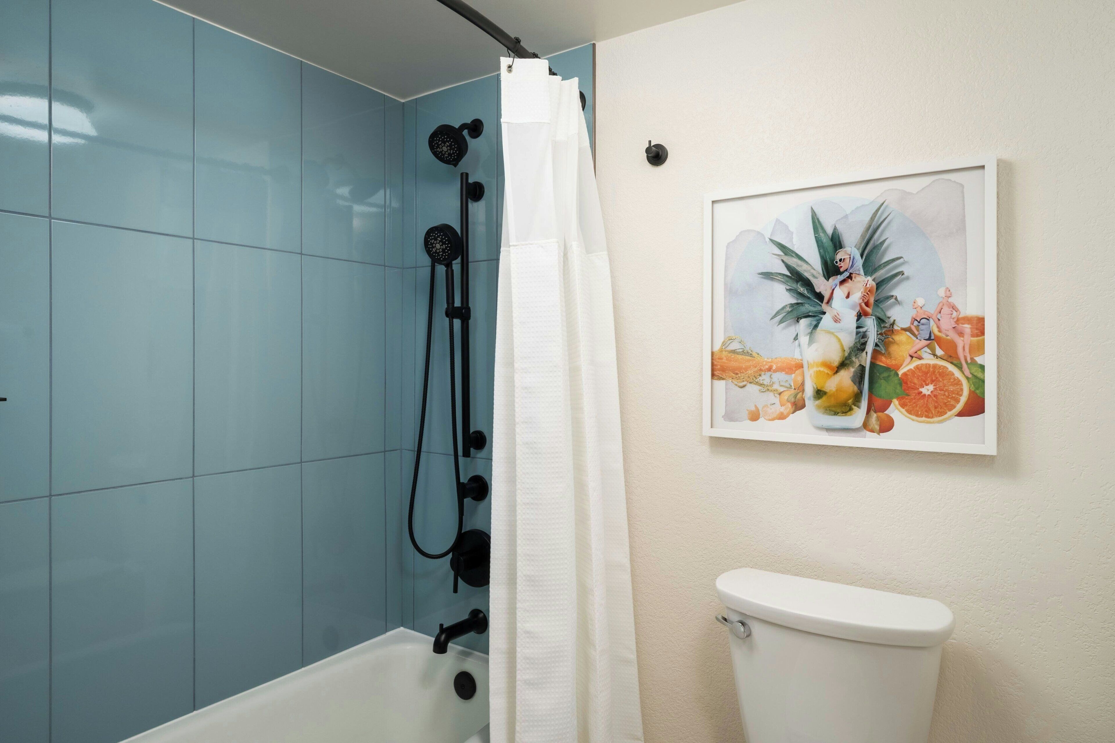 A bathroom with a shower, toilet, and a wall-mounted picture of fruits.