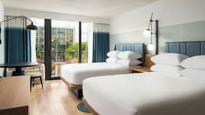Une chambre d’hôtel avec deux lits, un bureau et un balcon offrant une vue sur les bâtiments et la verdure.