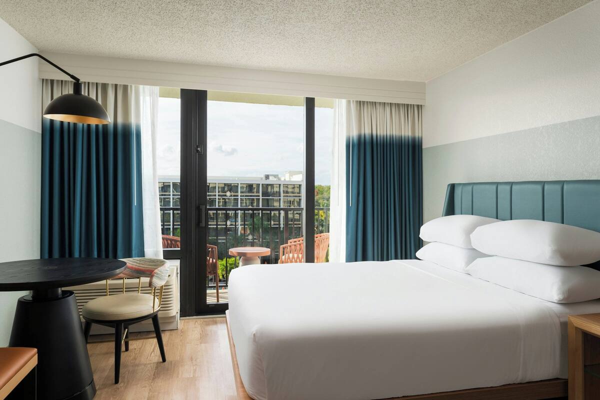 A hotel room with a bed, a desk, a chair, and a view of the outdoors.