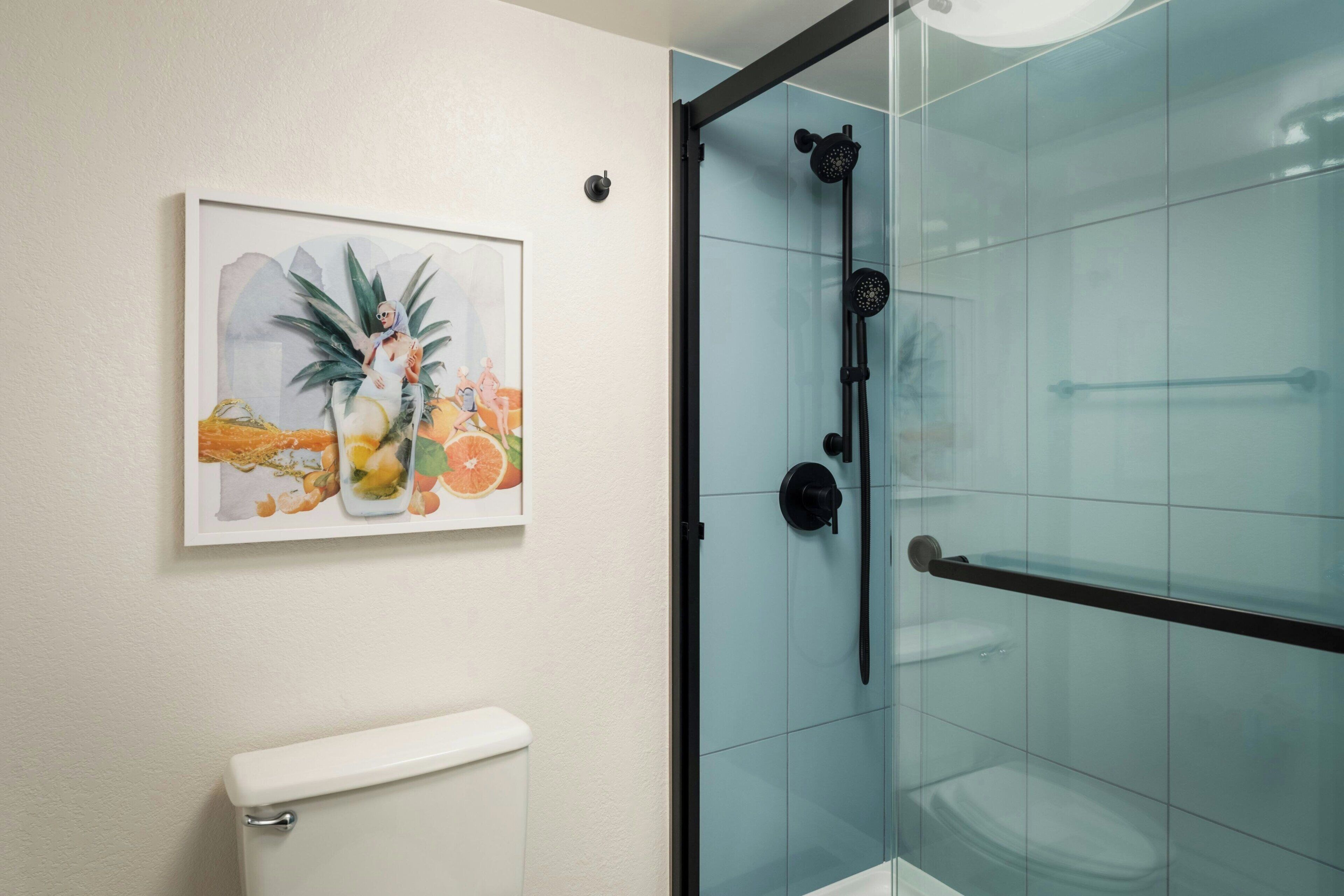 A bathroom with a glass shower enclosure, a toilet, and a framed artwork on the wall.