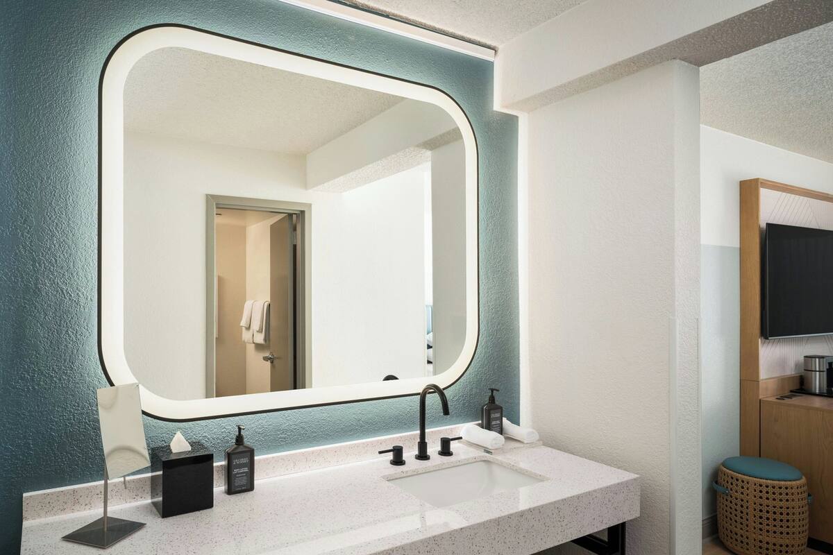 A modern bathroom with a large mirror, a white sink, and a wooden cabinet.