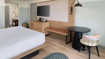 Ein modernes Hotelzimmer mit Bett, Schreibtisch, Stuhl, Fernseher und rundem Tisch.