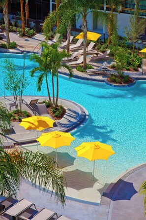 A swimming pool with sun loungers and yellow umbrellas, surrounded by palm trees and a building in the background. - Sheraton Orlando Lake Buena Vista Resort - NEWLY RENOVATED! (Orlando)