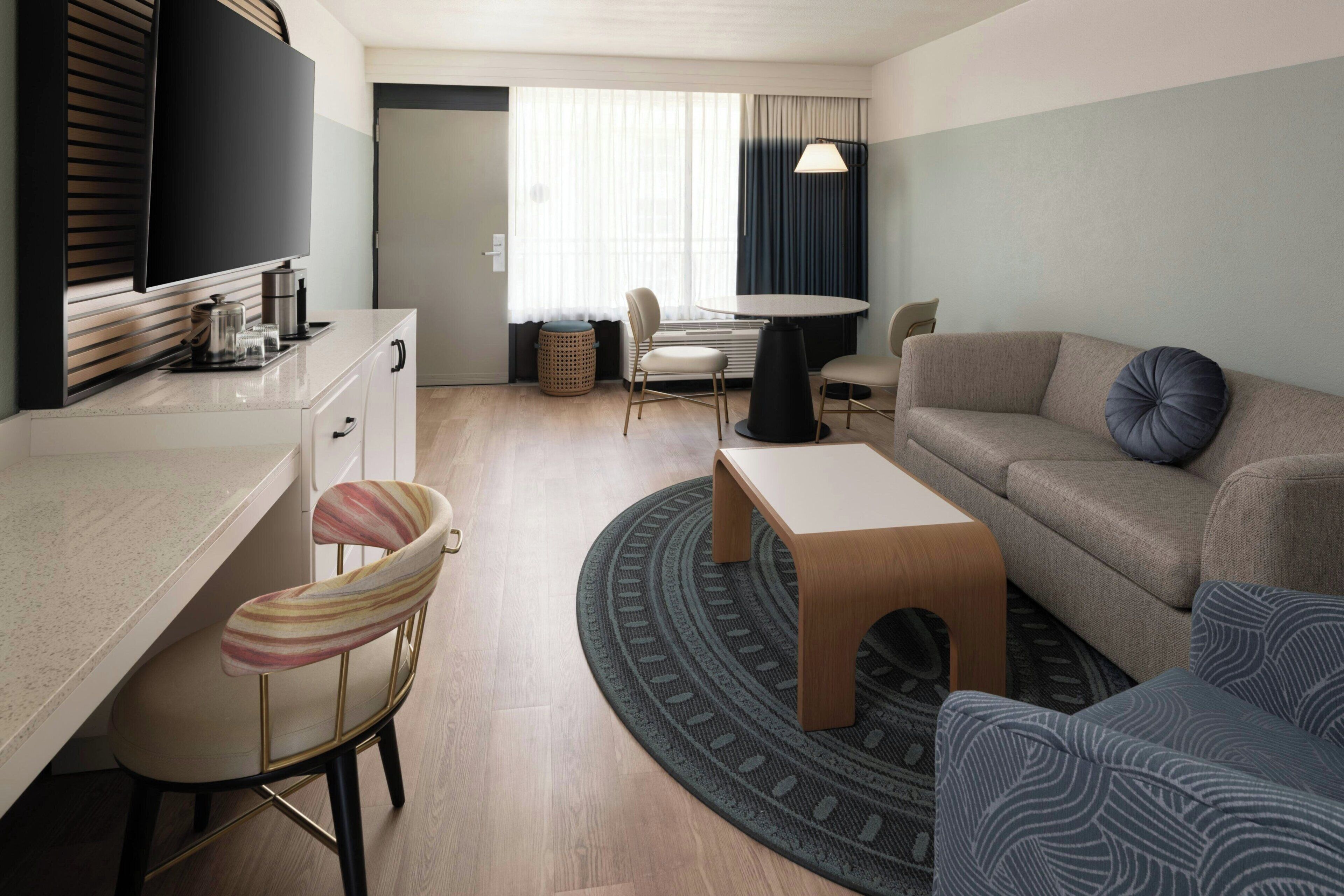 Una habitación de hotel moderna con kitchenette, un sofá, una mesa de comedor y un televisor.