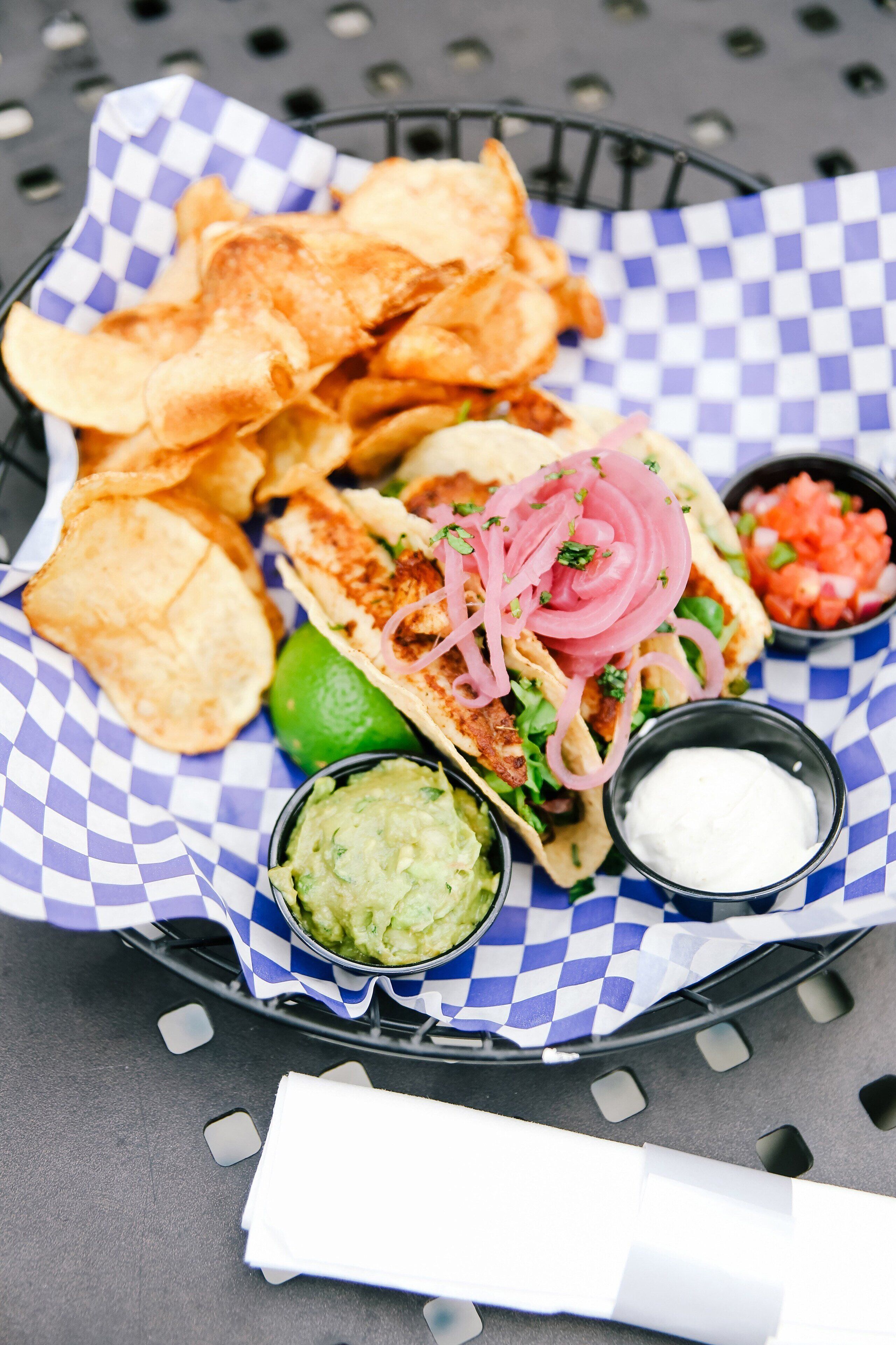 Uma cesta com tacos, guacamole, creme azedo e batatas fritas.